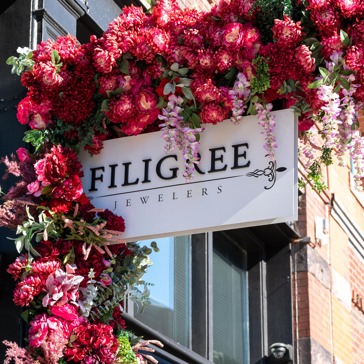 Filigree Jewelers’ storefront sign framed by pink and red flowers